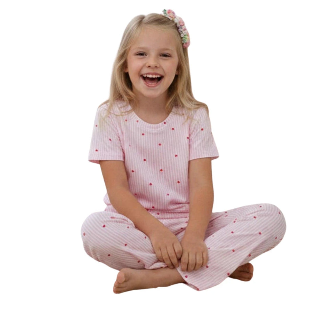 Young girl wearing a light pink striped cotton pyjama set with short sleeves and matching full-length pants featuring small polka dot details.