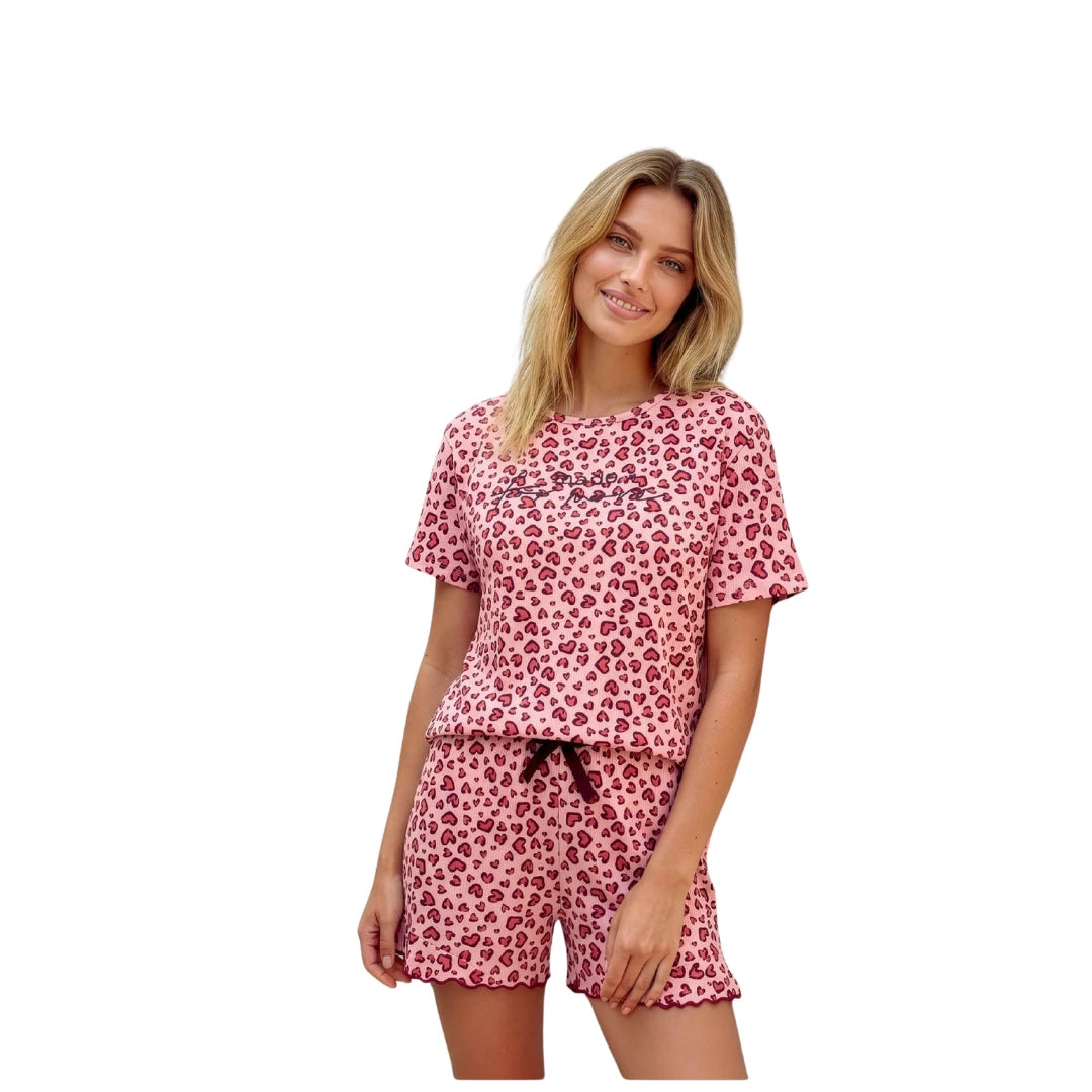 Woman wearing a pink heart print cotton pajama set with short sleeve top and matching shorts.