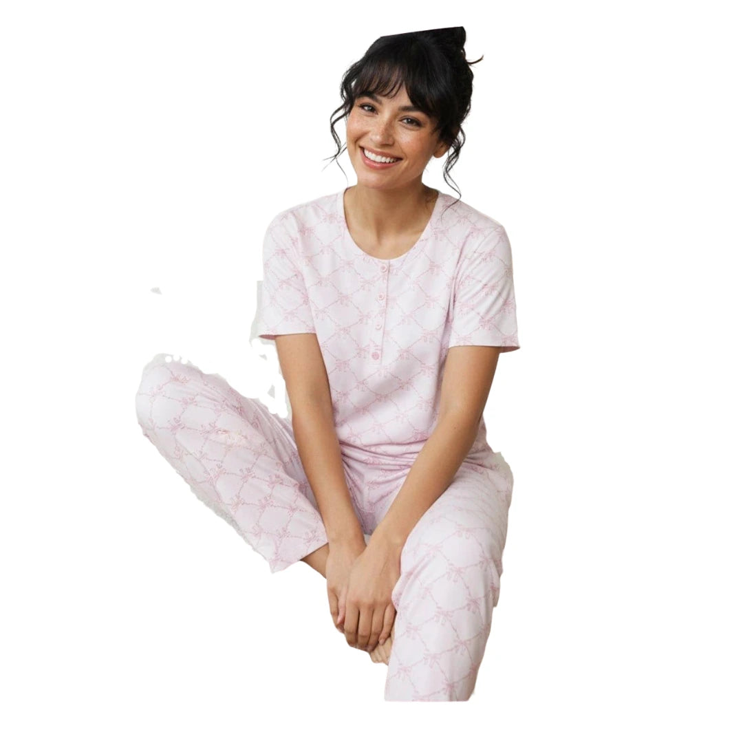 Woman wearing a light pink cotton pyjama set with a button-neck short-sleeve top and matching full-length printed pants on a white background.
