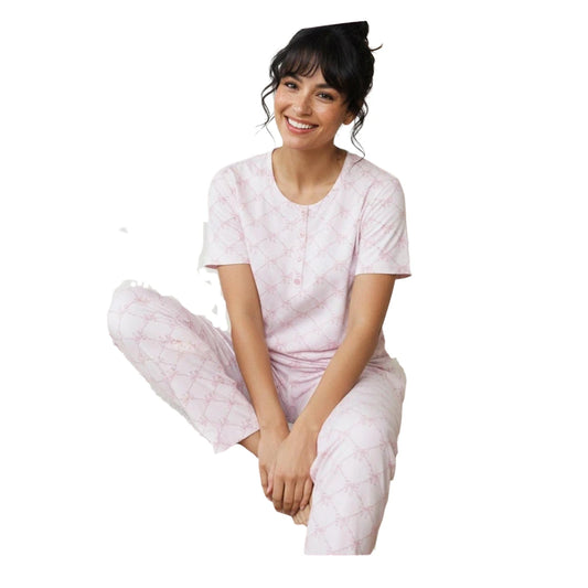 Woman wearing a light pink cotton pyjama set with a button-neck short-sleeve top and matching full-length printed pants on a white background.