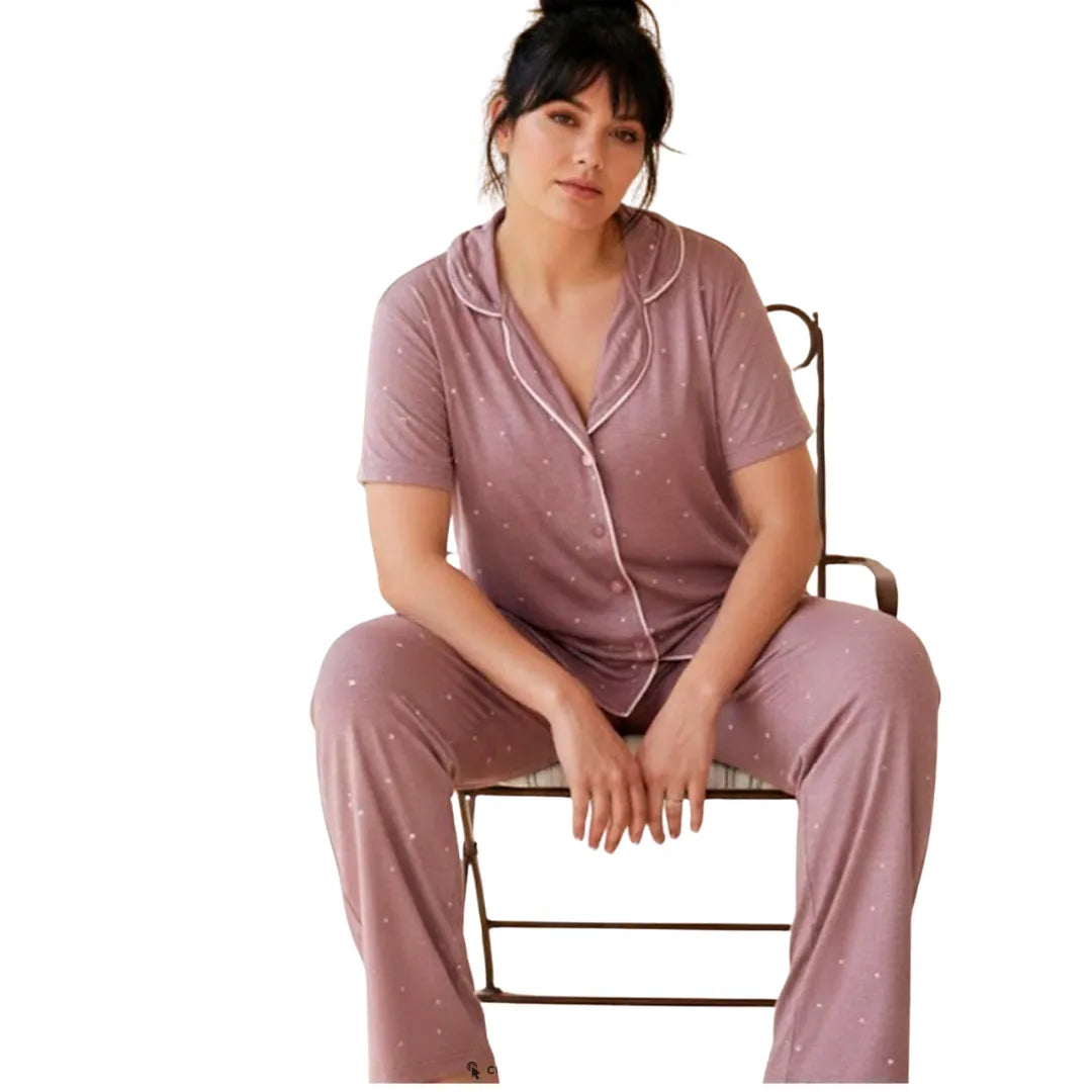 Woman wearing a soft mauve short sleeve button-up pajama set with white polka dots and full-length pants.