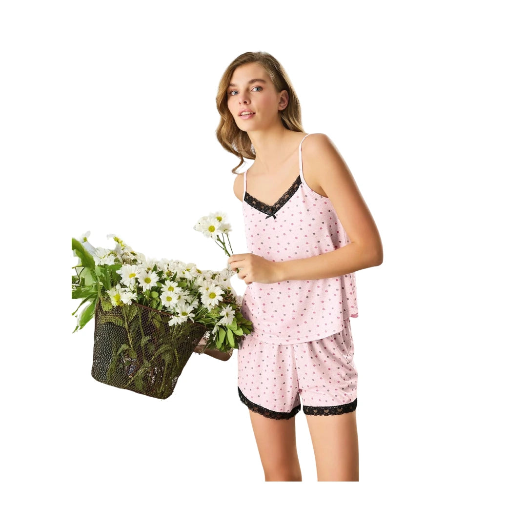 Woman wearing a soft pink 100% cotton camisole and shorts pyjama set with black lace trim and delicate polka dot print on a white background.