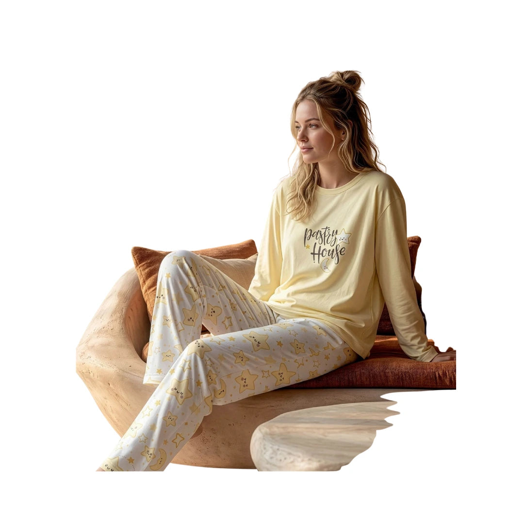 Woman wearing a soft yellow 100% cotton long sleeve pyjama set with a printed "Pastry House" top and matching white star-print lounge pants on a white background.